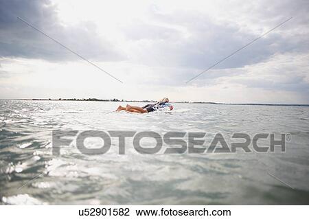Stock Image - Senior woman on surfboard in sea, paddleboarding. Fotosearch
