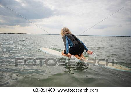 Stock Image - Senior woman on surfboard in sea, paddleboarding. Fotosearch