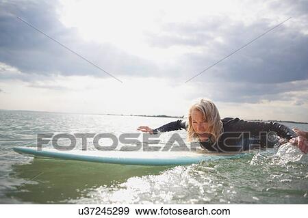 Stock Photo - Senior woman on surfboard in sea, paddleboarding. Fotosearch