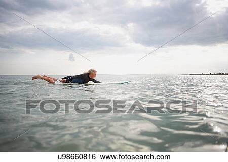Stock Photograph - Senior woman on surfboard in sea, paddleboarding. Fotosearch