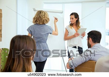 Stock Image - Senior woman presenting to design team in office. Fotosearch