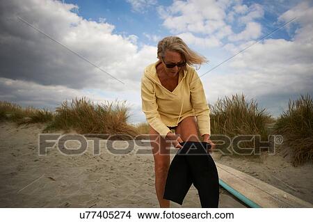 Picture - Senior woman putting on wetsuit. Fotosearch