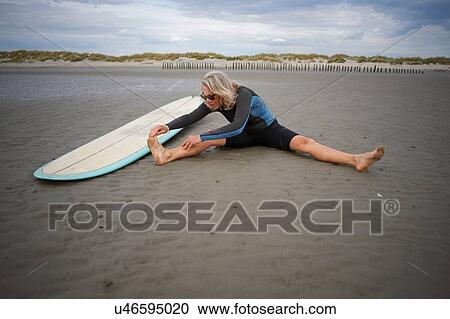 Senior woman sitting on sand, stretching, surfboard beside her View Large Photo Image Stock Image - Senior woman sitting on sand, stretching, surfboard beside her. Fotosearch