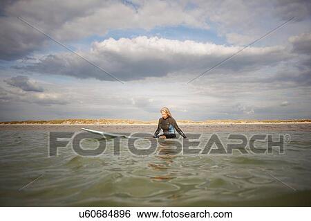 Stock Photograph - Senior woman sitting on surfboard in sea. Fotosearch