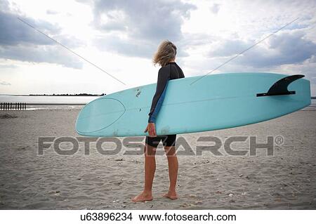 Senior woman standing on beach, holding surfboard, rear view View Large Photo Image Picture - Senior woman standing on beach, holding surfboard, rear view. Fotosearch