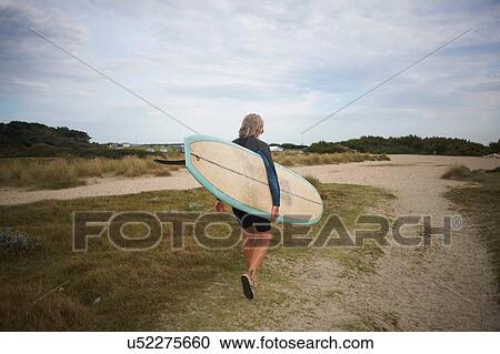 Senior woman walking along beach, carrying surfboard, rear view View Large Photo Image Stock Image - Senior woman walking along beach, carrying surfboard, rear view. Fotosearch