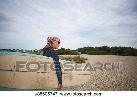 Senior woman walking along beach, carrying surfboard, rear view View Large Photo Image Stock Photo - Senior woman walking along beach, carrying surfboard, rear view. Fotosearch
