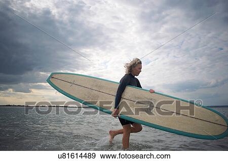 Senior woman walking from sea, carrying surboard View Large Photo Image Stock Photo - Senior woman walking from sea, carrying surboard. Fotosearch