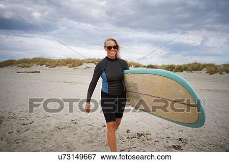 Senior woman walking on beach, carrying surboard View Large Photo Image Stock Photo - Senior woman walking on beach, carrying surboard. Fotosearch