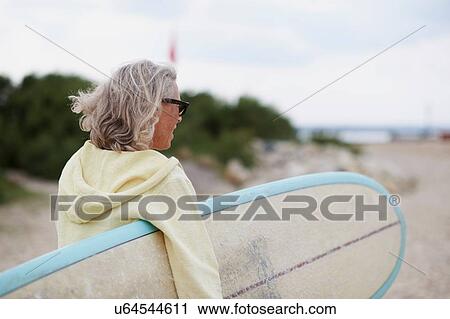 Senior woman walking towards beach, carrying surfboard, rear view View Large Photo Image Stock Image - Senior woman walking towards beach, carrying surfboard, rear view. Fotosearch
