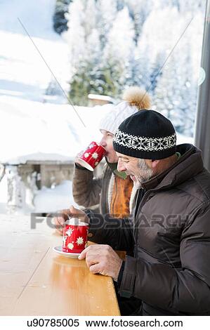 Stock Photography - Side view of senior couple sitting at table drinking hot chocolate, Sattelbergalm, Tyrol, Austria. Fotosearch