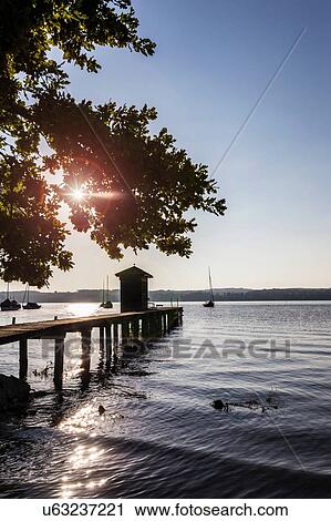 Stock Image - Silhouette of boathouse and pier at lake, Schondorf, Ammersee, Bavaria, Germany. Fotosearch