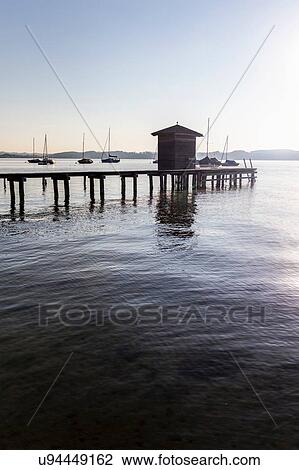 Stock Image - Silhouette of boathouse and pier at lake, Schondorf, Ammersee, Bavaria, Germany. Fotosearch