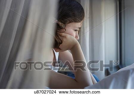 Picture - Sullen girl reclining on bed resting on elbow. Fotosearch