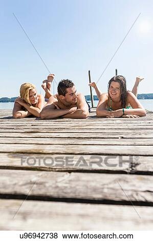 Surface level view of friends lying on front on wood pier sunbathing, Schondorf, Ammersee, Bavaria, Germany View Large Photo Image Stock Photo - Surface level view of friends lying on front on wood pier sunbathing, Schondorf, Ammersee, Bavaria, Germany. Fotosearch