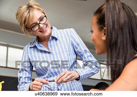 Teacher helping female student in classroom View Large Photo Image Stock Photo - Teacher helping female student in classroom. Fotosearch