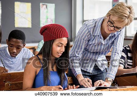 Teacher helping female student in classroom View Large Photo Image Stock Photo - Teacher helping female student in classroom. Fotosearch
