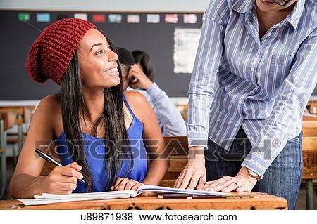 Stock Photo - Teacher helping female student in classroom. Fotosearch