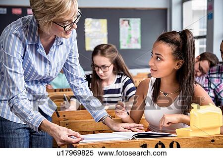Stock Photography - Teacher helping female student in classroom. Fotosearch