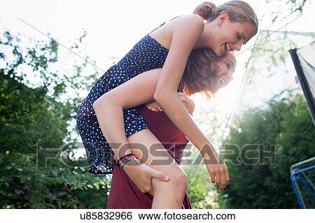 Teenage girl giving best friend a piggy back in park View Large Photo Image Stock Photograph - Teenage girl giving best friend a piggy back in park. Fotosearch