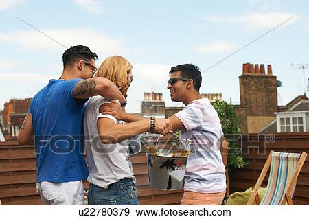 Three male friends carrying ice bucket with bottled beer at rooftop party View Large Photo Image Stock Photo - Three male friends carrying ice bucket with bottled beer at rooftop party. Fotosearch