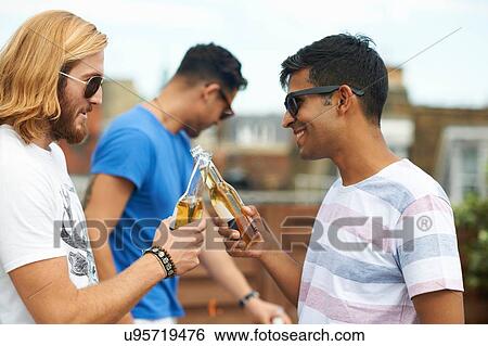 Two male friends making a toast with bottled beer at rooftop party View Large Photo Image Stock Photograph - Two male friends making a toast with bottled beer at rooftop party. Fotosearch