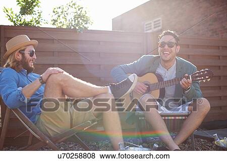 Two male friends playing guitar at rooftop party View Large Photo Image Stock Photo - Two male friends playing guitar at rooftop party. Fotosearch