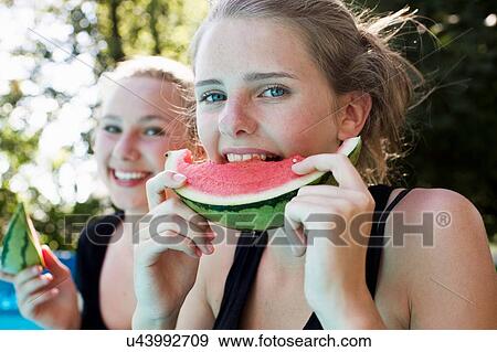 Two teenage girls eating watermelon slices in garden View Large Photo Image Stock Photo - Two teenage girls eating watermelon slices in garden. Fotosearch