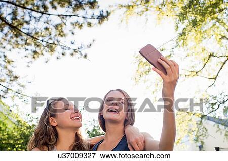 Stock Photo - Two teenage girls in park taking smartphone selfie. Fotosearch