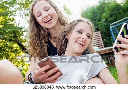 Stock Image - Two teenage girls reading smartphone texts in garden. Fotosearch