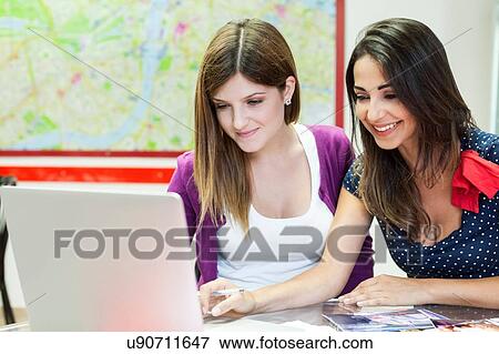Stock Photo - Two young women sitting together, studying, using laptop. Fotosearch