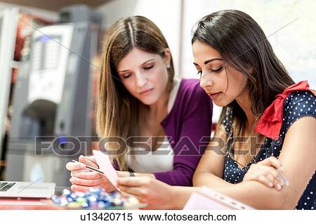 Two young women sitting together, studying View Large Photo Image Stock Photography - Two young women sitting together, studying. Fotosearch