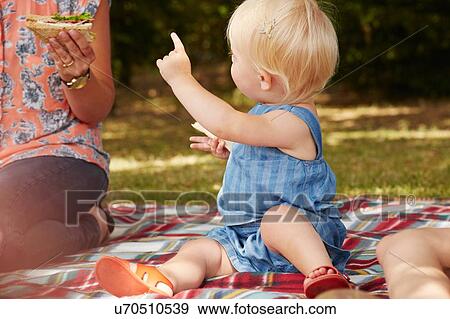 Stock Photo - Woman and baby girl sitting on picnic blanket having picnic. Fotosearch