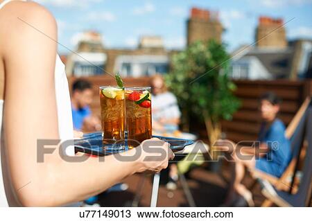 Stock Image - Woman carrying tray of cocktails at rooftop party. Fotosearch