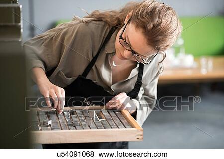 Stock Photo - Woman choosing letterpress from tray in print workshop. Fotosearch