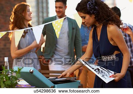 Stock Photograph - Woman putting on music at early evening party. Fotosearch