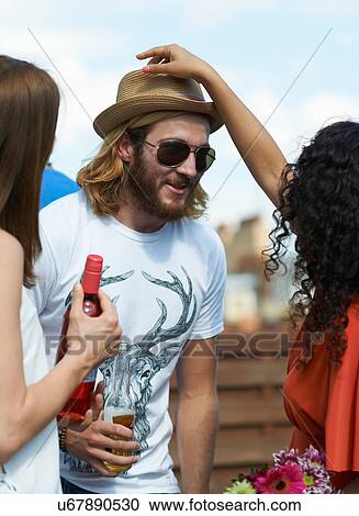 Woman putting straw hat on male friend at rooftop party View Large Photo Image Stock Image - Woman putting straw hat on male friend at rooftop party. Fotosearch
