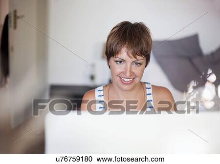 Stock Image - Woman using computer in bedroom. Fotosearch