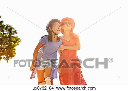 Picture - Woman with arm around rollerblading daughter in sunlight. Fotosearch