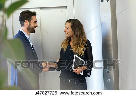 Stock Photograph - Young businessman and woman shaking hands at elevator. Fotosearch