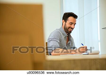 Stock Photograph - Young businessman making notes at boardroom table. Fotosearch
