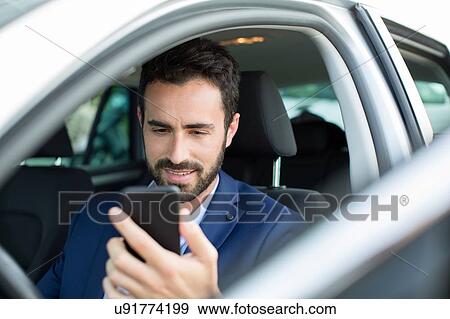 Young businessman reading smartphone texts in car View Large Photo Image Stock Photo - Young businessman reading smartphone texts in car. Fotosearch