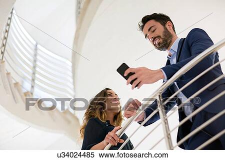 Young businessman reading smartphone texts on office stairway View Large Photo Image Stock Photography - Young businessman reading smartphone texts on office stairway. Fotosearch