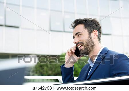 Young businessman talking on smartphone outside office View Large Photo Image Stock Image - Young businessman talking on smartphone outside office. Fotosearch