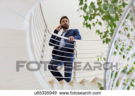 Stock Photo - Young businessman talking on smartphone on office stairway. Fotosearch