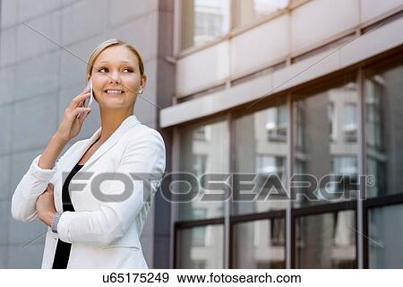 Stock Photo - Young businesswoman chatting on smartphone outside office. Fotosearch