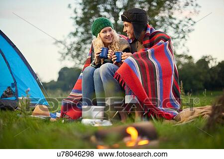 Stock Photo - Young camping couple sitting by campfire with cup of tea. Fotosearch