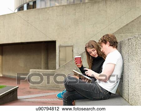 Stock Image - Young couple having coffee, using smartphone on concrete bench, Melbourne, Victoria, Australia. Fotosearch