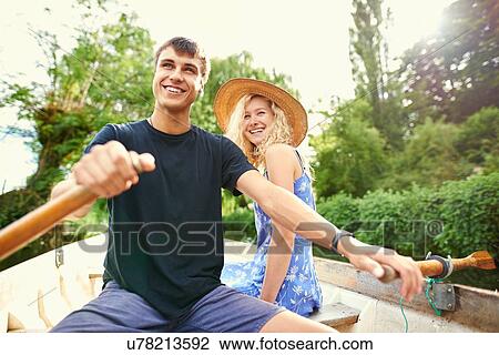 Stock Image - Young couple rowing boat on rural river. Fotosearch
