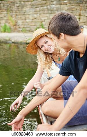 Stock Image - Young couple touching water from rowing boat on rural river. Fotosearch